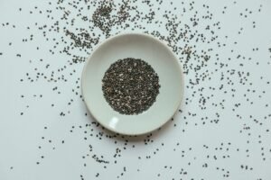 Top view of chia seeds in a white bowl with scattered seeds around on a flat surface.