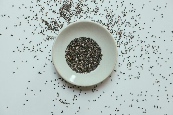 Top view of chia seeds in a white bowl with scattered seeds around on a flat surface.